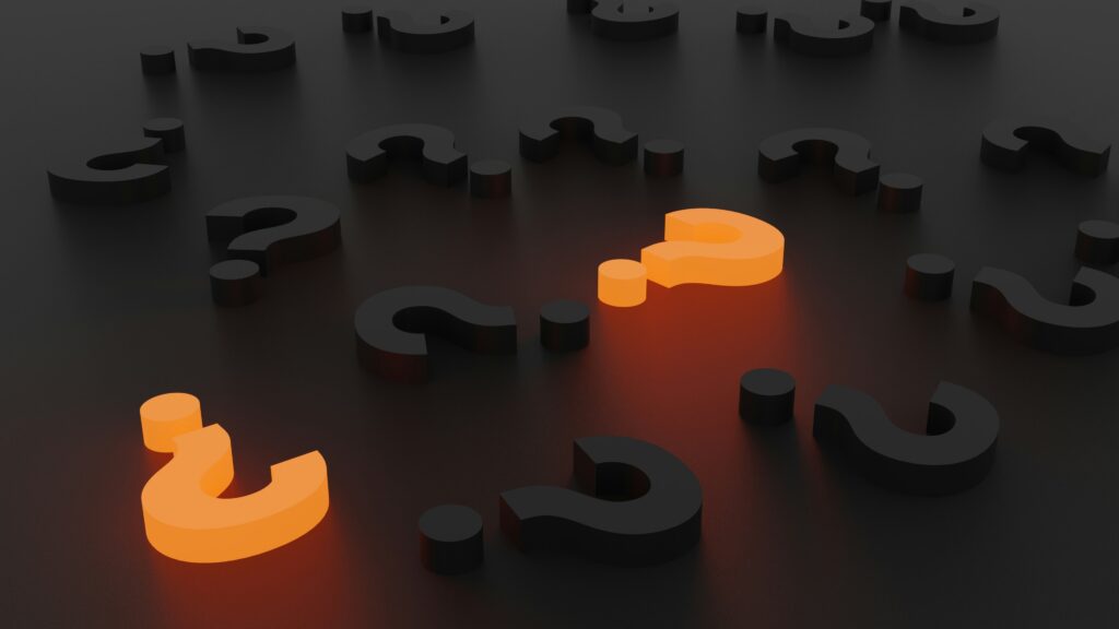 neon question marks among black question marks laid out on a dark table top